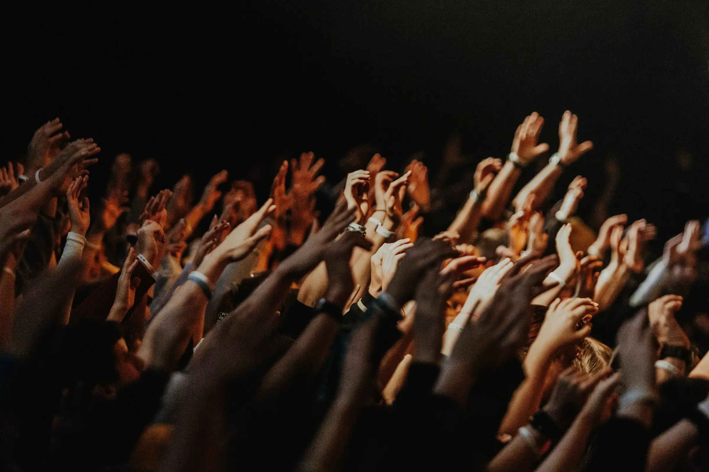 Mãos levantadas em adoração durante um culto, sob luz quente